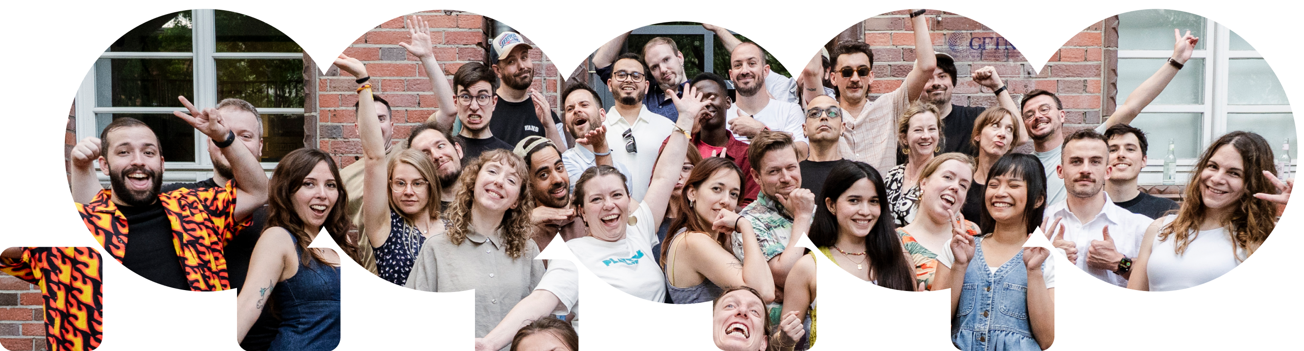 A diverse group of happy adults posing energetically in front of a brick wall and windows.