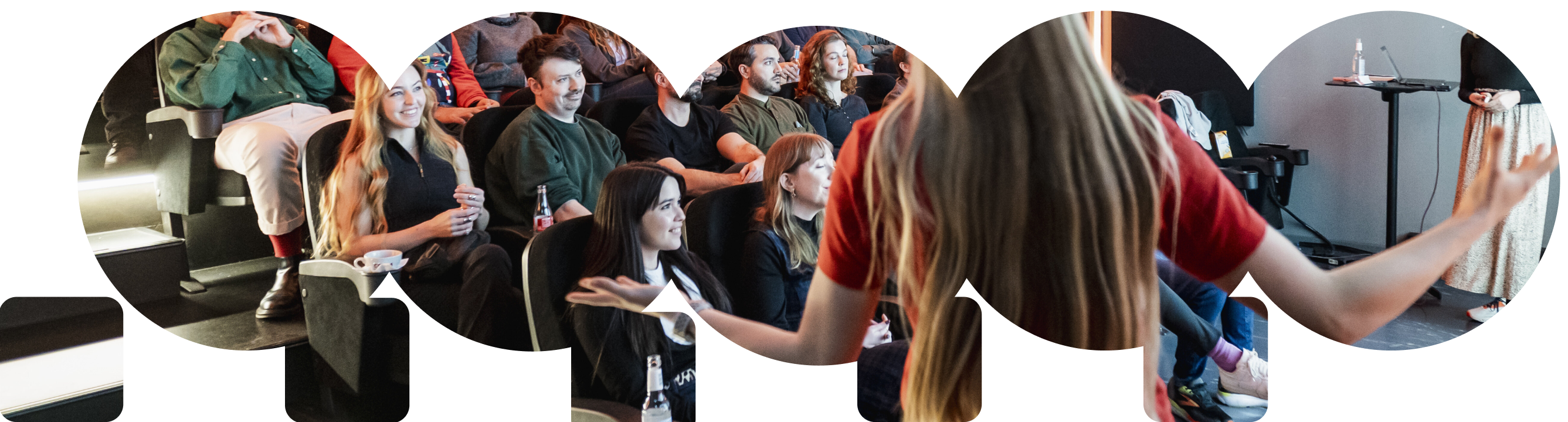 Audience attentively listening to a speaker in a casual indoor setting, with a woman in a red shirt presenting in the foreground.
