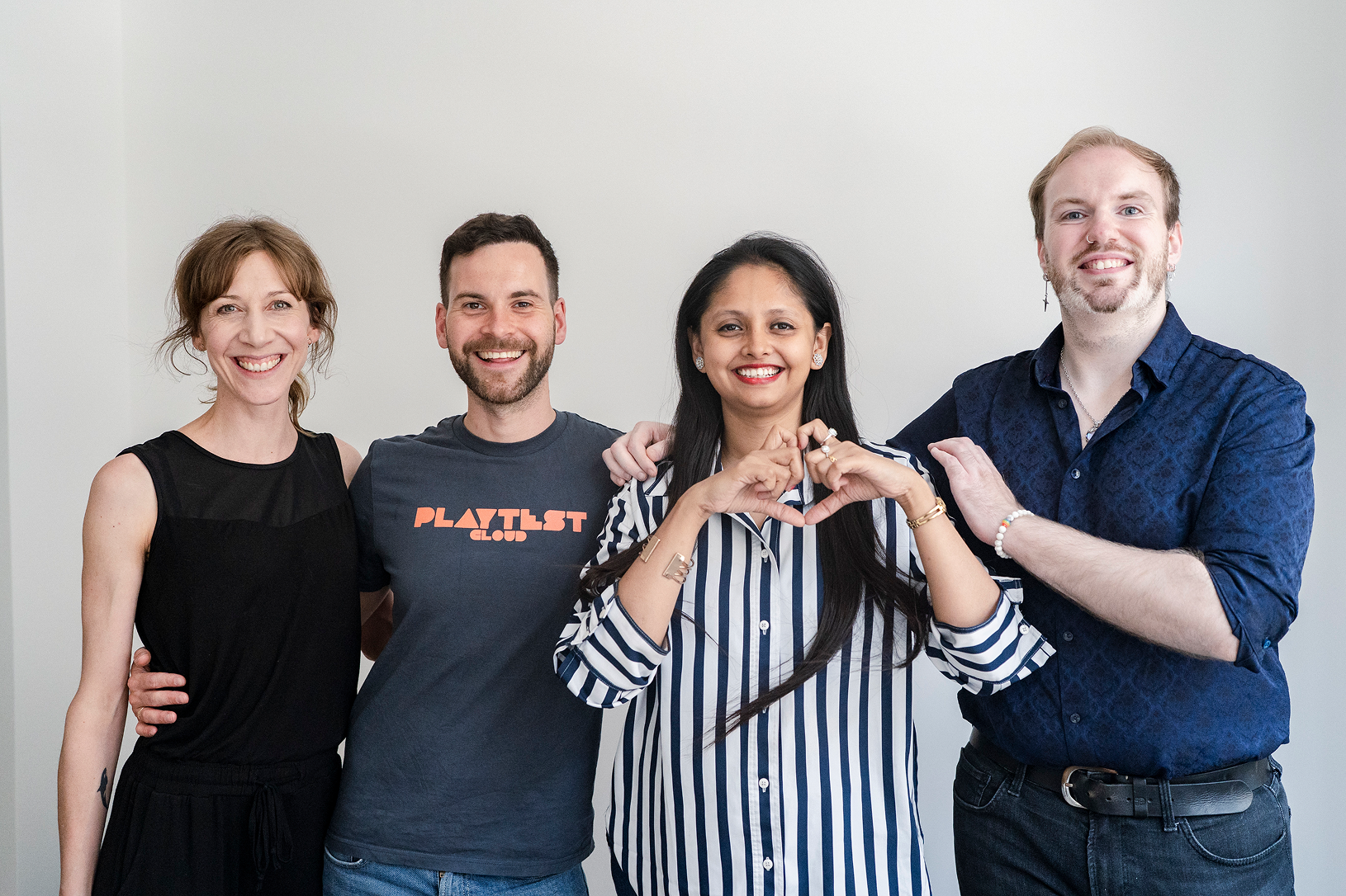 Four smiling colleagues standing side by side with one woman forming a heart shape with her hands.